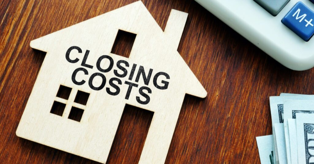 Wooden house model with "CLOSING COSTS" text, calculator, and cash on wooden surface, illustrating financial aspects of buying a home in Guelph.