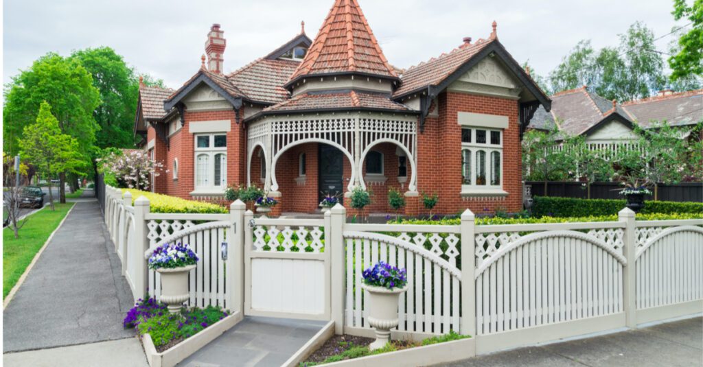 Heritage-style red brick house with a distinctive turret, decorative porch, and manicured garden, showcasing unique architectural features relevant to Guelph real estate.
