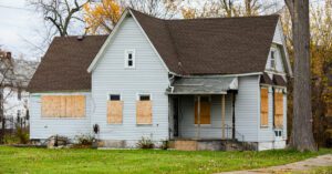 Abandoned blue house with boarded windows and overgrown yard, illustrating challenges in Guelph real estate market.