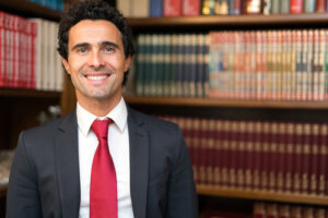 Smiling professional man in a suit and red tie standing in front of a bookshelf filled with legal books, representing expertise in real estate law for Guelph home selling.